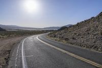 a motorcycle riding down a winding highway between hills and dry grass on a sunny day