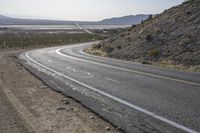 a motorcycle riding down a winding highway between hills and dry grass on a sunny day