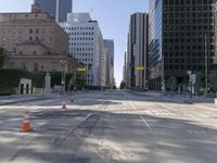 the empty road has an orange traffic cone along it near some tall buildings in downtown san diego