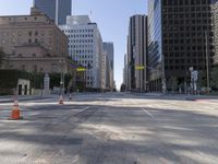 the empty road has an orange traffic cone along it near some tall buildings in downtown san diego