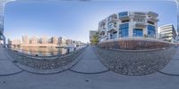 a street and a body of water with some buildings in the background, in a 360 - view lens