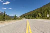 a deserted highway in the mountains with pine trees and mountains in the background, taken from the front seat