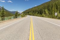 a deserted highway in the mountains with pine trees and mountains in the background, taken from the front seat