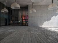 two lamps hanging on a concrete wall over a brick floor in a public space with concrete flooring