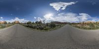 a wide view of a paved road in the desert with rocks in the background with trees and bushes