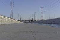 a road leading to a bridge with water running underneath it and power lines in the background