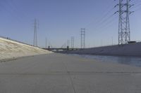 a road leading to a bridge with water running underneath it and power lines in the background