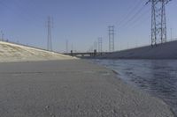 a road leading to a bridge with water running underneath it and power lines in the background