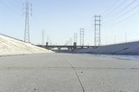 a road leading to a bridge with water running underneath it and power lines in the background