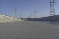 a road leading to a bridge with water running underneath it and power lines in the background