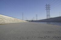 a road leading to a bridge with water running underneath it and power lines in the background