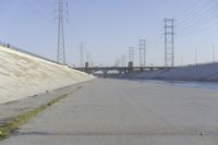 a road leading to a bridge with water running underneath it and power lines in the background