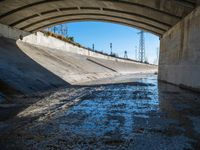 there is water under a highway bridge and in the middle the road is mud, and the other side of the river