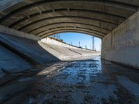 there is water under a highway bridge and in the middle the road is mud, and the other side of the river