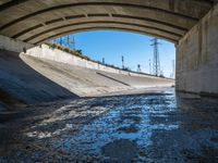 there is water under a highway bridge and in the middle the road is mud, and the other side of the river