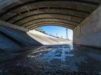 there is water under a highway bridge and in the middle the road is mud, and the other side of the river