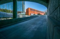 an empty walkway leads out to a building in the distance with other buildings and tall towers in the background