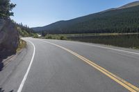 two yellow lines on road beside mountain and lake as seen from vehicle point of view