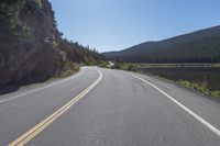 two yellow lines on road beside mountain and lake as seen from vehicle point of view