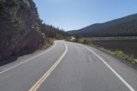 two yellow lines on road beside mountain and lake as seen from vehicle point of view