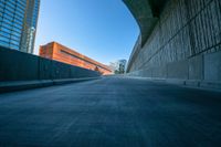 an empty road and a wall with several buildings in the background behind it are blue skies