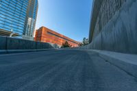 an empty road and a wall with several buildings in the background behind it are blue skies