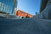 an empty road and a wall with several buildings in the background behind it are blue skies