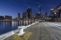 the lights shine brightly at night along a pier overlooking water and buildings in the distance