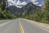 there are three lanes that are empty in the road next to the mountains with trees and bushes