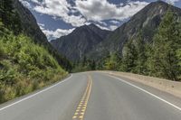 there are three lanes that are empty in the road next to the mountains with trees and bushes