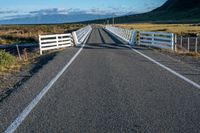 an empty road with a fence leading over the side of it and mountains in the distance