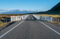 an empty road with a fence leading over the side of it and mountains in the distance