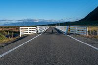 an empty road with a fence leading over the side of it and mountains in the distance