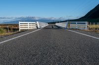 an empty road with a fence leading over the side of it and mountains in the distance