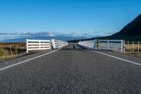 an empty road with a fence leading over the side of it and mountains in the distance