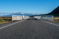 an empty road with a fence leading over the side of it and mountains in the distance