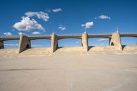 a concrete structure with arches and pillars near an asphalt field with a blue sky above it