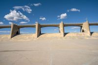 a concrete structure with arches and pillars near an asphalt field with a blue sky above it