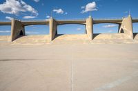 a concrete structure with arches and pillars near an asphalt field with a blue sky above it