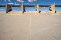 a concrete structure with arches and pillars near an asphalt field with a blue sky above it