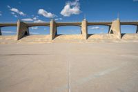 a concrete structure with arches and pillars near an asphalt field with a blue sky above it