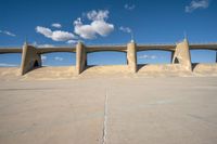 a concrete structure with arches and pillars near an asphalt field with a blue sky above it