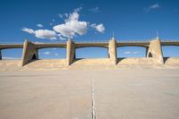 a concrete structure with arches and pillars near an asphalt field with a blue sky above it