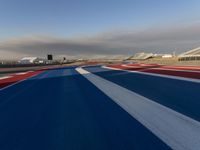 a racing track with red, white and blue stripes and a passenger plane in the background