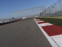 red and white track lines next to silver metal poles with green grass in front of blue sky