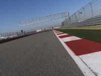 red and white track lines next to silver metal poles with green grass in front of blue sky