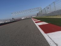 red and white track lines next to silver metal poles with green grass in front of blue sky