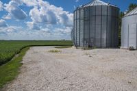there is a large cement silo with several grain bins in the background that also has a sky filled with white clouds