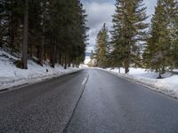 an empty road surrounded by snow and trees in the winter time, near a mountain