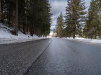 an empty road surrounded by snow and trees in the winter time, near a mountain